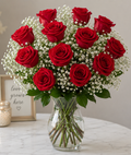 Bouquet of red roses with baby's breath in a clear vase on a marble surface.
